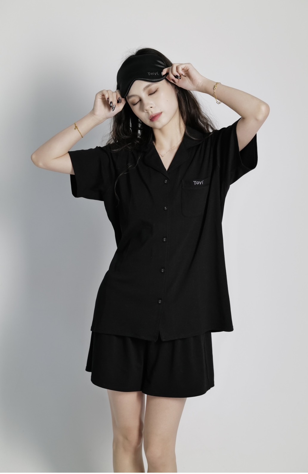 Model in black Tovi sleepwear easing a sleep mask over closed eyes